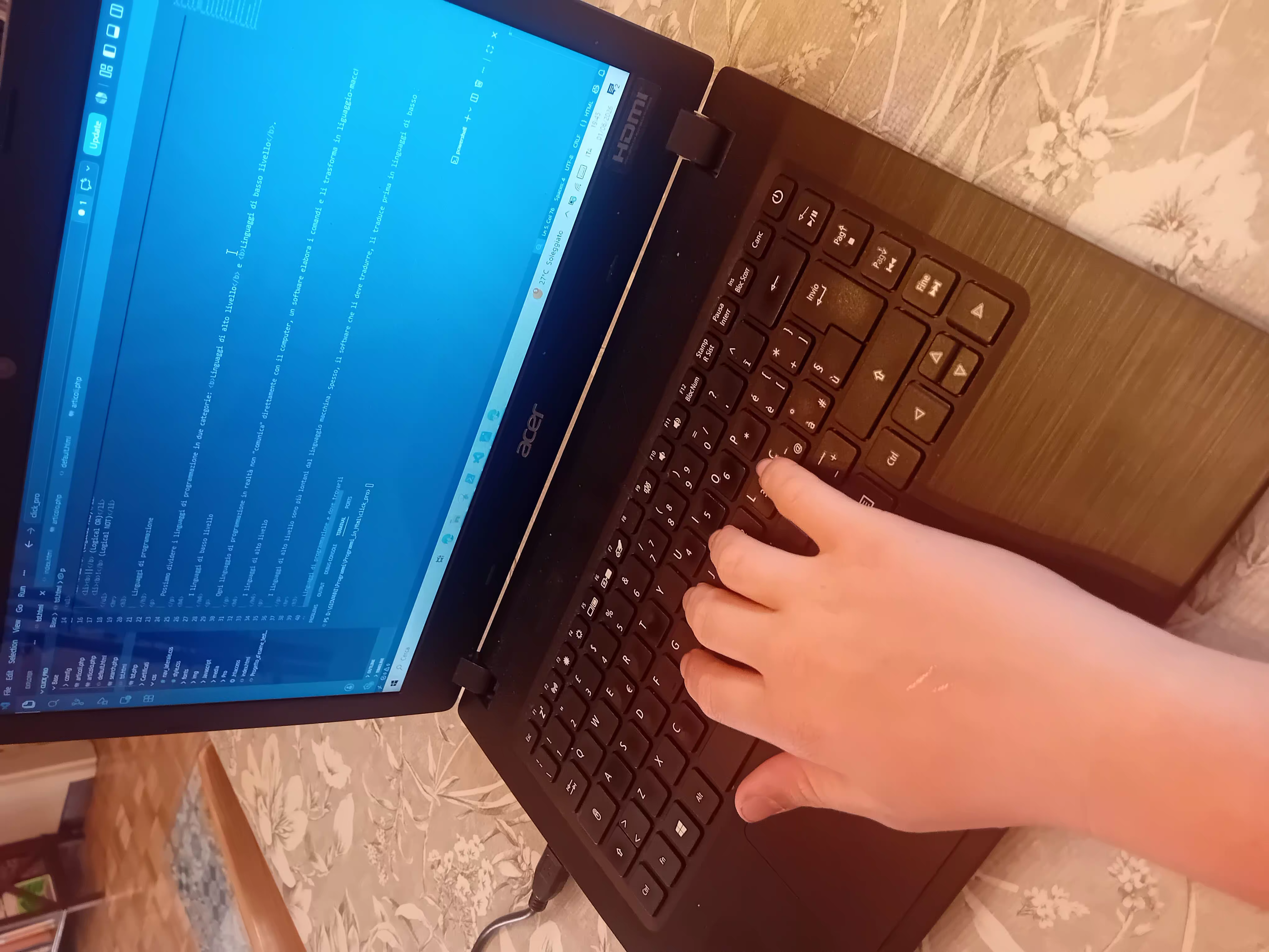 Immagine di un dito che preme un tasto sulla tastiera di un laptop. Sullo schermo dello stesso è aperto VSCode con il codice di una pagina web